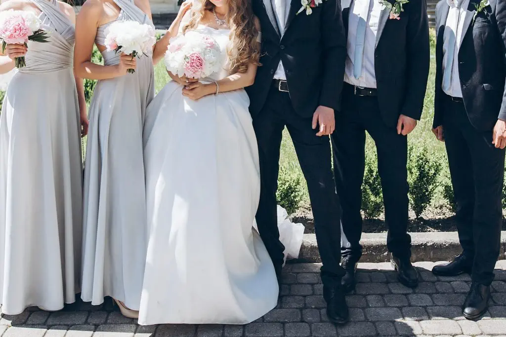 Bride and groom posing in sunny garden with bridesmaids and groomsmen