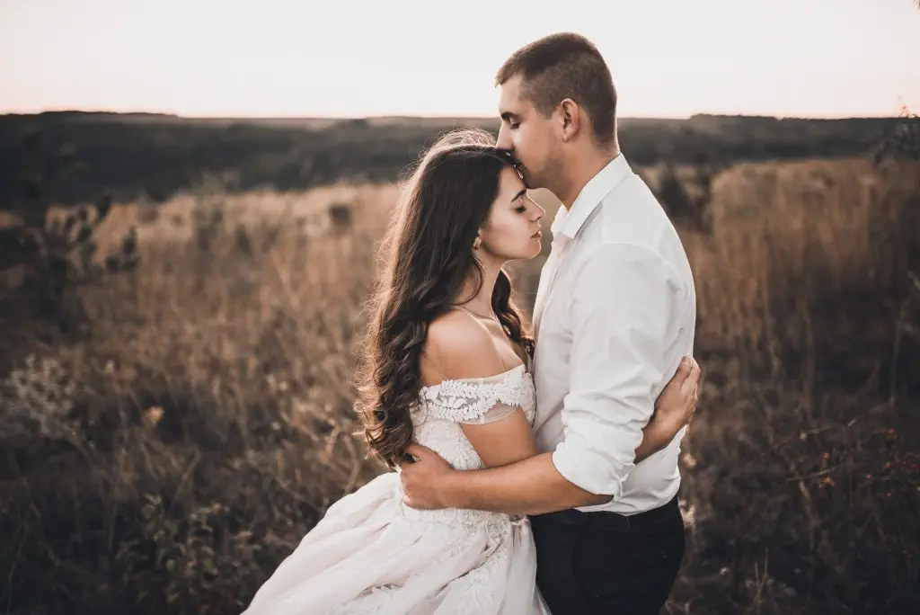 bride and groom walking on the meadow in summer at sunset