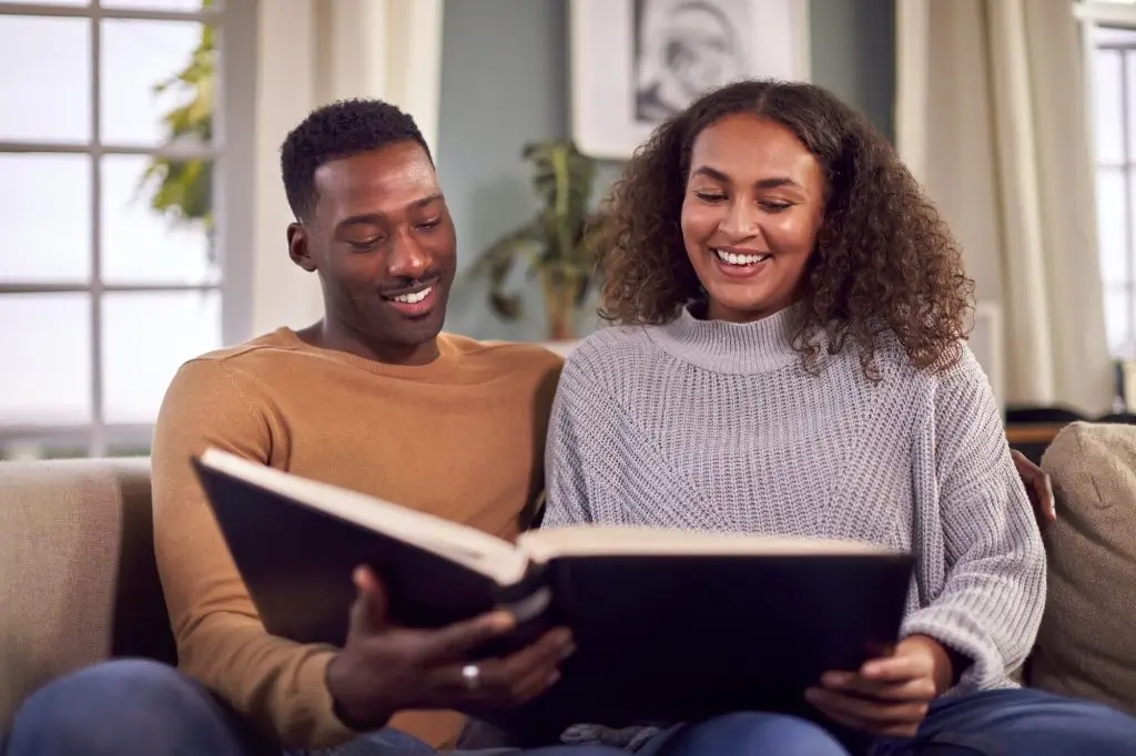 Smiling Couple Sitting On Sofa At Home Looking Through Photo Album
