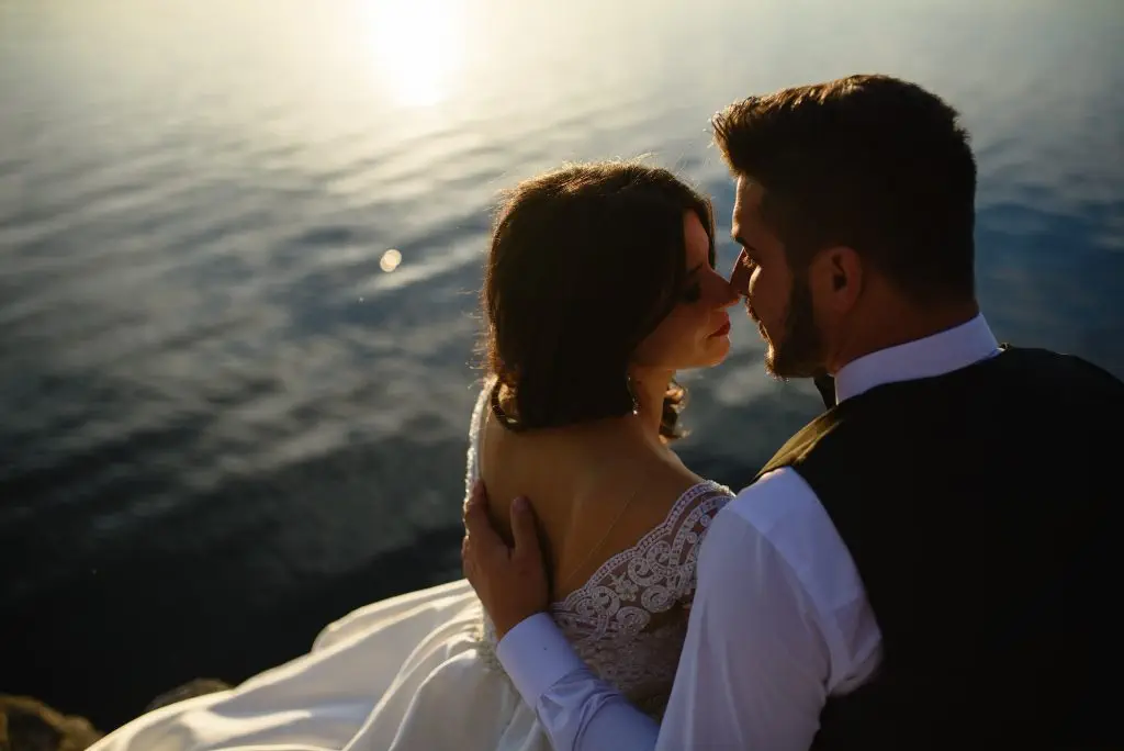 The bride and groom are sitting on the edge of a cliff against the backdrop of the lake.